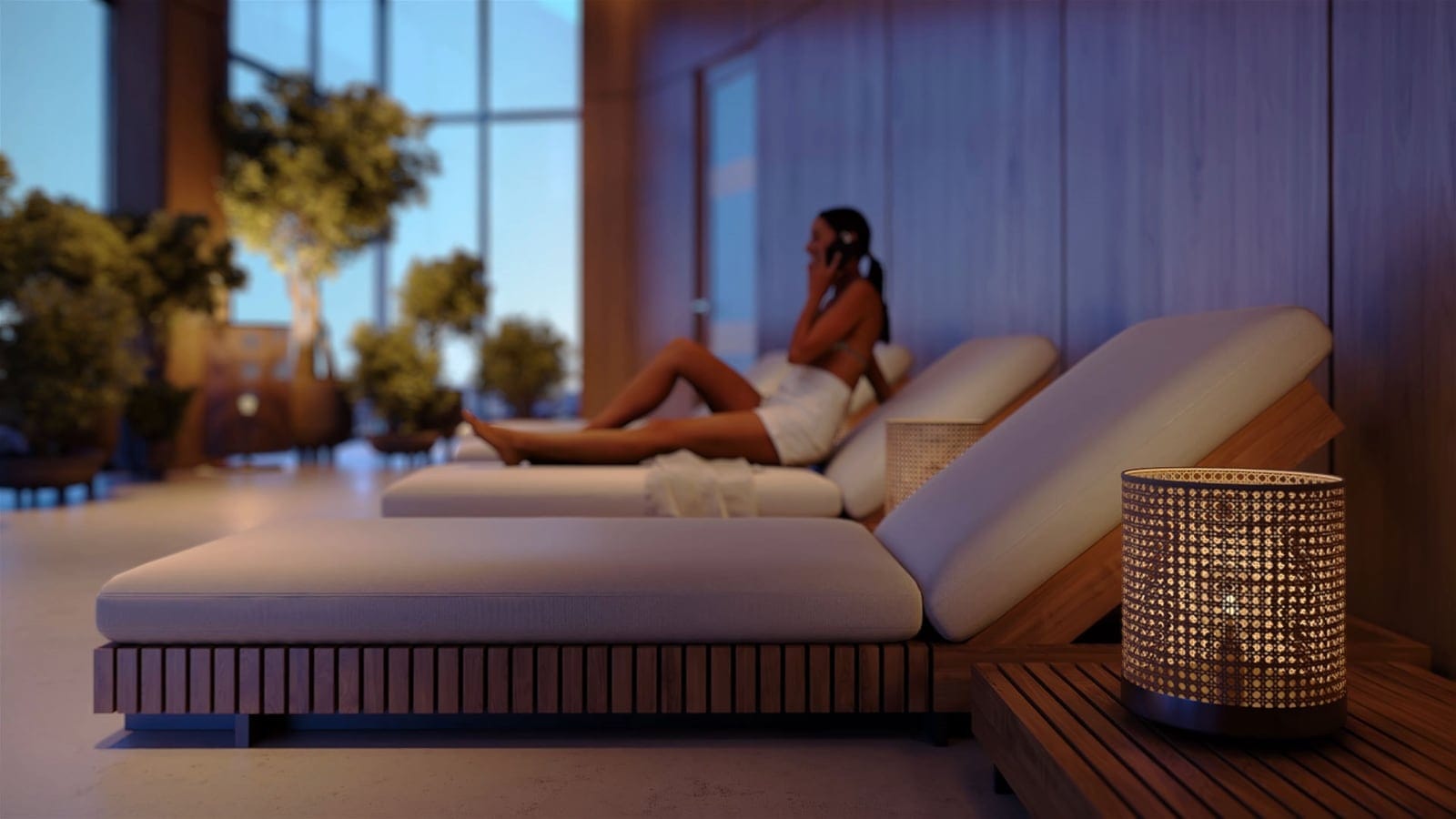 A woman resting on a lounger in the spa’s relaxation lounge, with plants and tall windows behind
